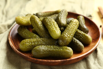 Wooden plate with tasty pickled cucumbers on yellow background