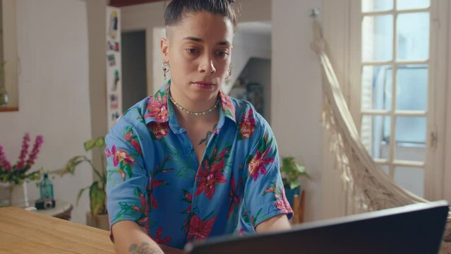 Young trendy girl with tattoos and piercing opening laptop and typing at desk with smartphone and ring light on it, preparing digital content for social media blog at home. Zoom Shot