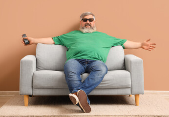 Mature man in 3D glasses watching TV on sofa near beige wall