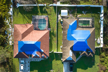 Aerial view of damaged in hurricane Ian house roof covered with blue protective tarp against rain...