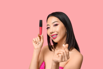Beautiful Asian woman with lipstick making heart with her fingers on pink background
