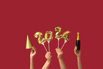 Female hands with champagne bottle, party hat and figure 2024 made of balloons on red background