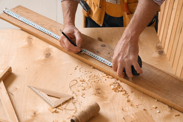 Mature carpenter measuring wooden plank at table in shop, closeup