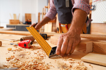 Mature carpenter measuring wooden plank at table in shop, closeup