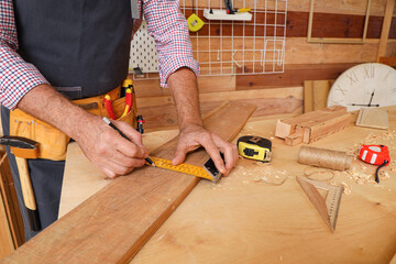 Mature carpenter measuring wooden plank at table in shop, closeup