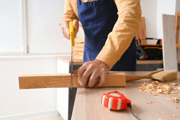 Mature carpenter sawing wooden plank at table in workshop, closeup - obrazy, fototapety, plakaty