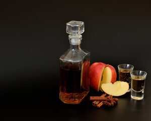 Homemade apple liqueur with cinnamon and anise in a bottle and two glasses on a black background.