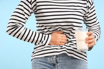Mature woman with glass of milk suffering from stomachache on blue background, closeup