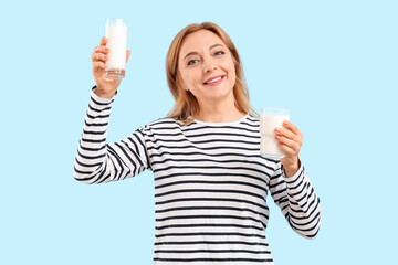 Mature woman with glasses of milk on blue background