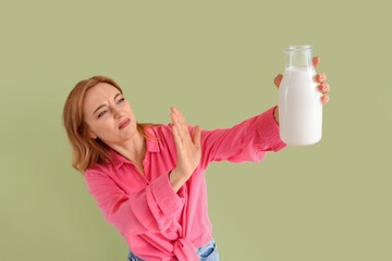 Displeased mature woman rejecting bottle of milk on green background
