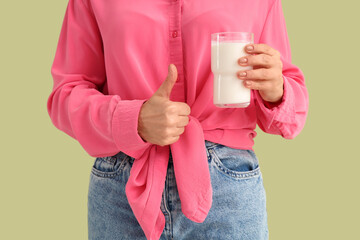 Mature woman with glass of milk showing thumb-up on green background, closeup