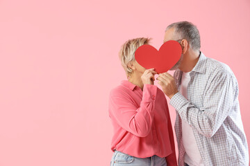 Mature couple with paper heart on pink background. Valentine's Day celebration