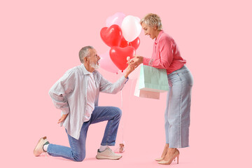 Mature man proposing to his beloved on pink background. Valentine's Day celebration