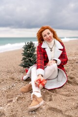 Lady in plaid shirt holding a gift in his hands enjoys beach with Christmas tree. Coastal area. Christmas, New Year holidays concep