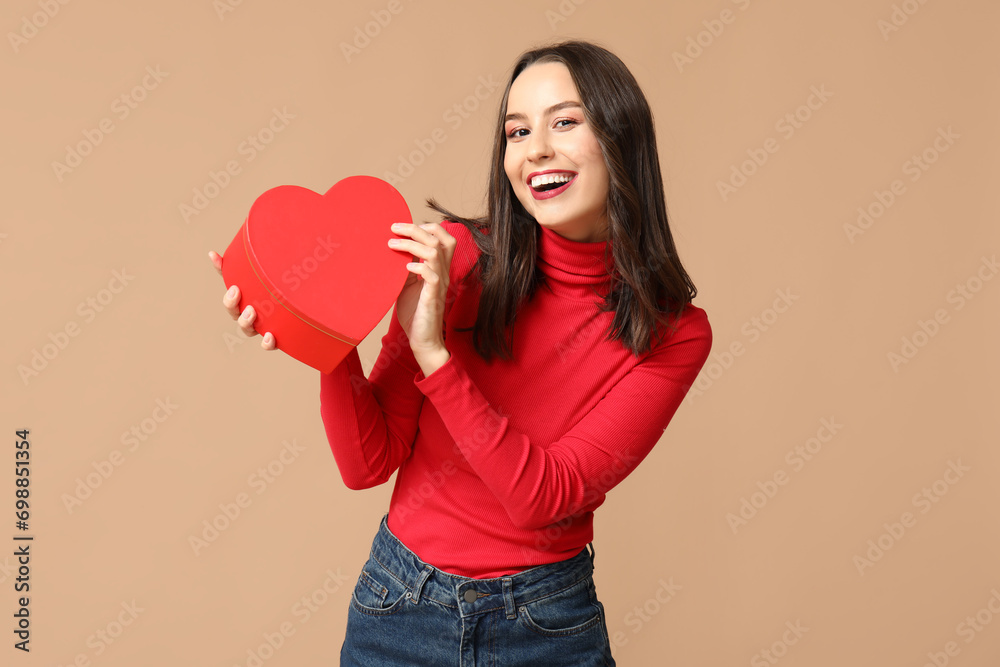 Wall mural happy young woman with gift box in shape of heart on brown background. valentine's day celebration