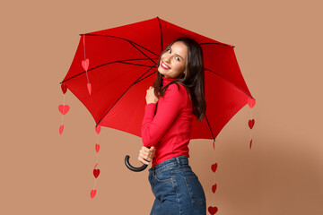 Beautiful young woman holding umbrella with paper hearts on brown background. Valentine's Day...