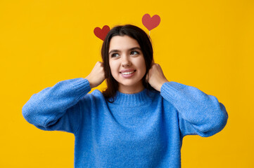 Beautiful young girl with red paper hearts on yellow background. Valentine's Day celebration