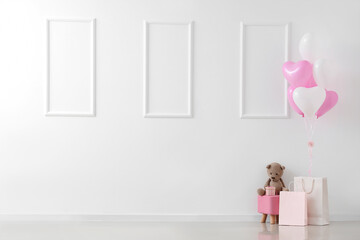 Pouf with teddy bear, shopping bags and heart-shaped balloons near white wall. Valentine's Day celebration