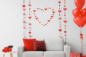 Interior of festive living room with grey sofa, heart-shaped balloons and decorative hearts....
