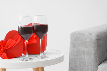 Glasses of wine and heart-shaped gift boxes on coffee table in living room, closeup. Valentine's...