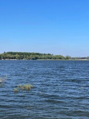 Beautiful riverscape on a windless early summer evening. The blue of the open river against the blue sky
