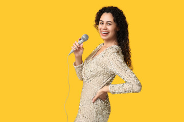 Beautiful young happy African-American female singer with microphone on yellow background