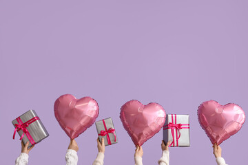 Female hands with gift boxes and heart shaped air balloons on lilac background. Valentine's Day...