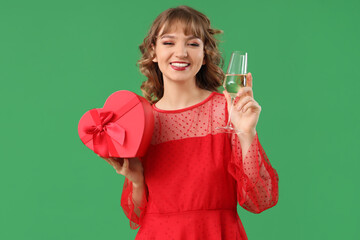 Beautiful young woman with glass of champagne and gift box on green background. Valentine's Day celebration