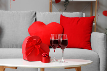 Heart-shaped gift boxes and glasses of wine on coffee table in living room. Valentine's Day...