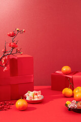 Tangerines, a plate of colorful gummy candy, a plate of jam and a red gift box are displayed on a lucky red background. Space for display and advertising.