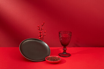 A black ceramic plate, a glass and a plate of melon seeds are displayed on a red background. Copy space for Tet advertising. Holiday theme with front view.