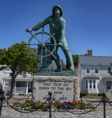 Bronze statue of a fisherman in oilskins standing braced at the wheel on the sloping deck of his...
