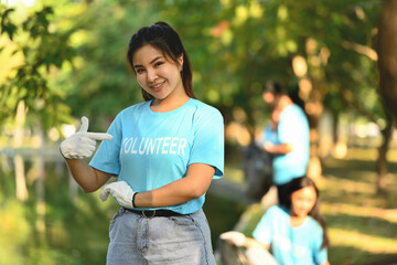 Young woman pointing to volunteer uniform while standing outdoor. Charity and community service concept.