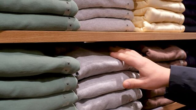 A male hand chooses clothes on shelves in the store close-up.