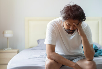 Depressed adult Asian man sitting in bed cannot sleep from insomnia.