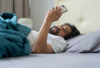 The serious Asian man lay on the bed and phone at morning in bed. Side view