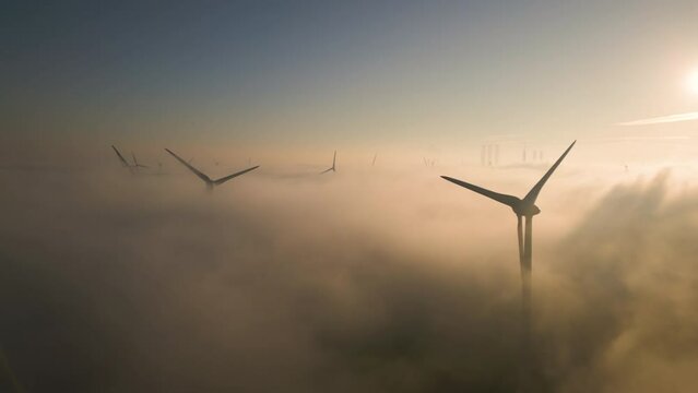 Cinematic aerial view of wind turbines in the misty sky at sunrise