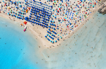 Aerial view of beautiful beach with white sand, colorful umbrellas, swimming people in blue sea at summer sunny day. La Pelosa beach, Sardinia, Italy. Top drone view of sandy beach, transparent water