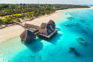 Fotobehang Aerial view of beautiful hotel on the water in ocean at sunset in summer. Zanzibar, Africa. Top view. Landscape with wooden hotel on the sea, azure water, sandy beach, green palm trees. Luxury resort © Prisicaruta