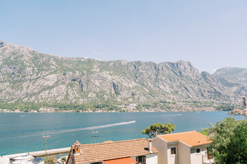 View over the red roofs of houses to a motor boat sailing on the sea against the backdrop of...