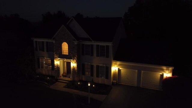 American Colonial two story home at night with garage and front porch lights on. Aerial push in shot.