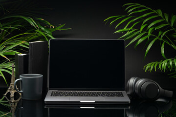 Laptop with black screen on working desk with cup and earphones on black background