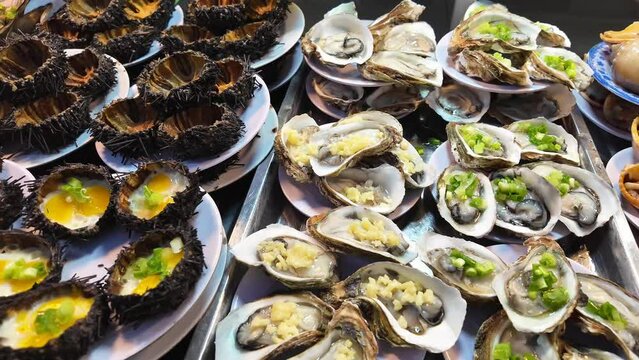 Assorted fresh sea urchins and oysters, some garnished with scallions and sauce, presented on plates at a seafood market