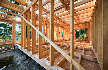 Under-construction residential wooden frame home located near a forest. Commencement of a new construction project for a cozy house or a mountain cottage. Idea of contemporary ecological construction. - obrazy, fototapety, plakaty