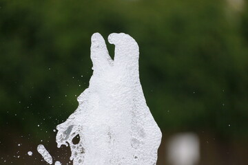 Water fountain geyser caught midair, white water foam frozen in time, foliage in unfocused...
