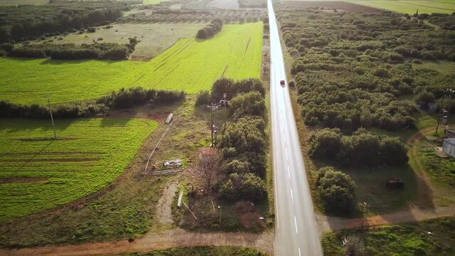 High drone shot of a car driving on a road passing through the fields at sunset in Tithorea, Greece