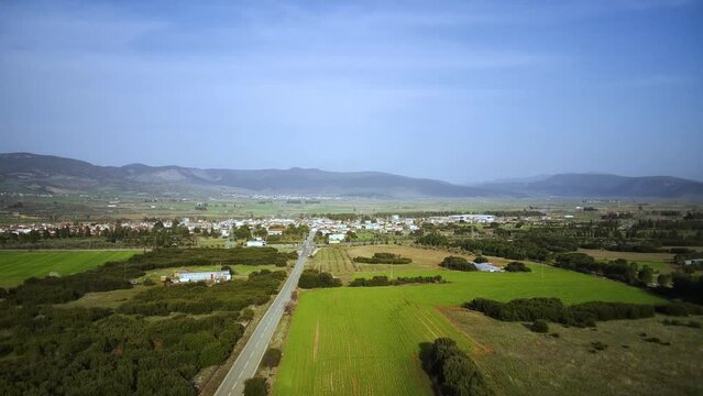 Drone shot of a road passing through green fields with Tithorea cityscaope in the background, Greece