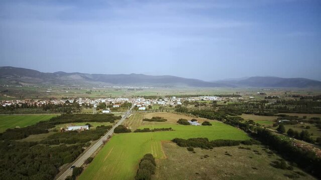 Aerial view of a car driving on road through green fields with the cityscape of Tithorea in Greece