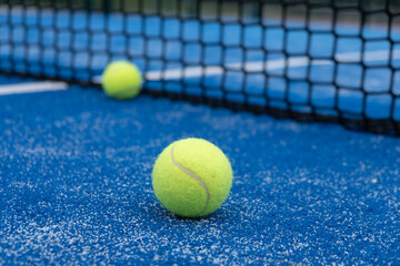 Two balls near the net of a blue padel tennis court, racket sports