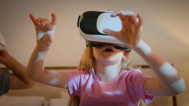Surprised Caucasian children kids boy girl brother sister friends siblings playing online video game in virtual reality glasses at home on bed play in world metaverse using innovative 3D VR headset